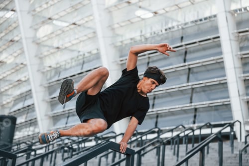 Preview: Does parkour. Young man in sportive clothes have workout outdoors at daytime
