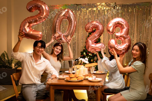 Preview: Young people holding 2023 pink gold balloon while toasting with champagne and enjoying celebrating