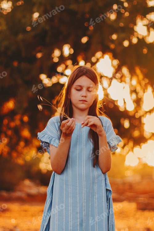 Preview: Little girl standing alone in warm sunset lights. Female wearing casual dress enjoy summer evening