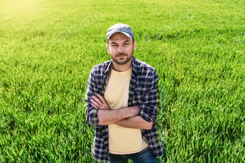 Preview: Man farmer in casual outfit near green agricultural field in spring