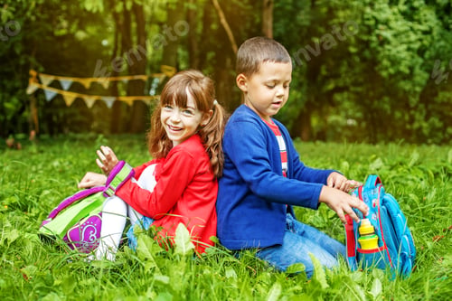Preview: Children sit on the grass. Schoolchildren with backpacks. The co