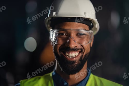 Preview: Happy young industrial man with protective wear indoors in metal workshop, looking at camera.