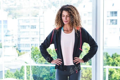 Preview: Confident woman in sportswear standing by window, enjoying urban city view
