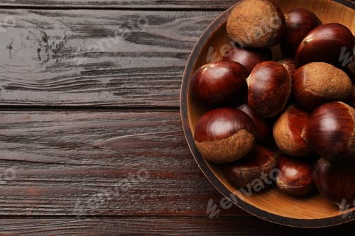 Preview: Sweet fresh edible chestnuts in bowl on wooden table, top view. Space for text