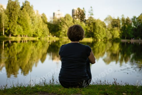 Preview: Adult woman sitting in the park on the grass in the rays of sunset Sunny