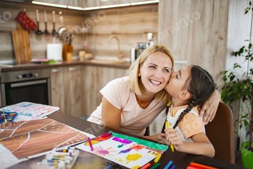 Preview: Cute girl kisses her mother while they both work on vibrant art projects