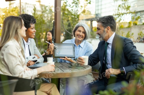 Preview: Business people having a meeting at outdoor cafe showing charts on tablet