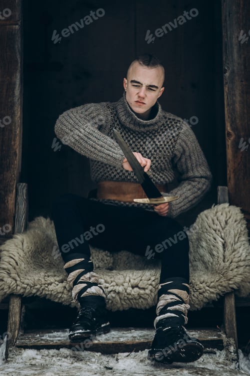 Preview: Portrait of strong viking warrior sharpening his sword, scandinavian viking cosplay