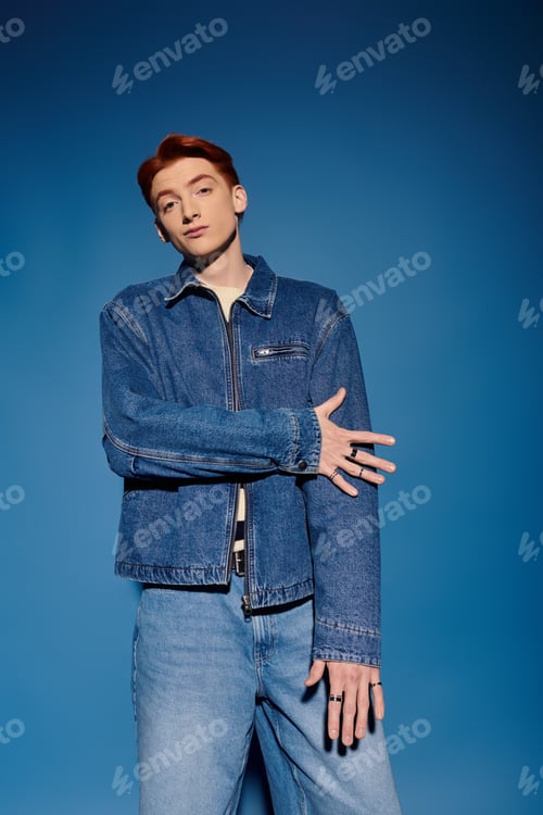 Preview: Emotional young man in denim jacket poses against a vibrant blue backdrop