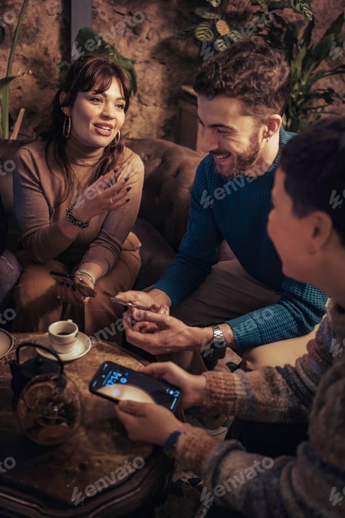 Preview: Friends Enjoying a Relaxed Evening with Drinks and Phones in a Cozy Cafe