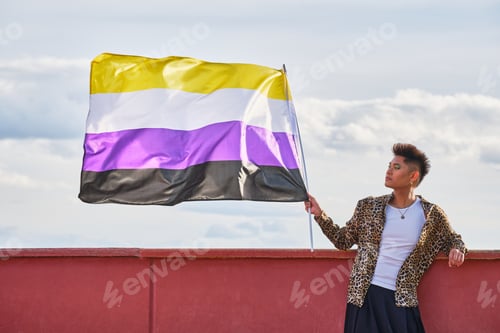 Preview: young gender non-binary asian person holding rainbow gay pride flag blowing in the wind