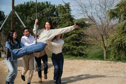 Preview: Friends pushing a young woman on a swing in a park
