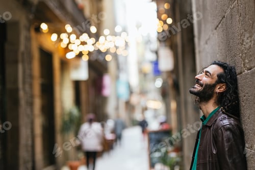 Preview: Young man leaning against a wall in a narrow street is laughing