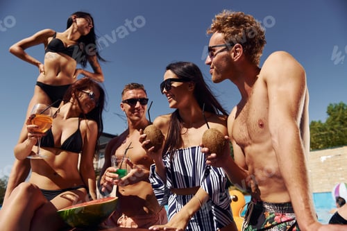 Preview: Holding watermelon. Group of young happy people have fun in swimming pool at daytime