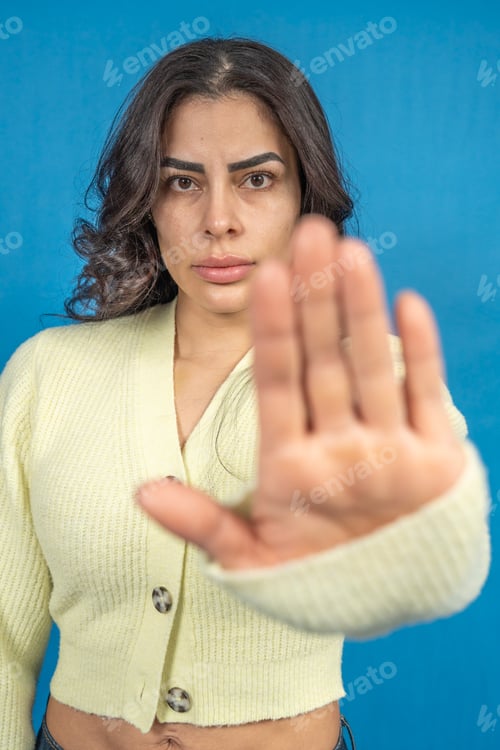Preview: Serious young woman making stop sign with hand, blue background