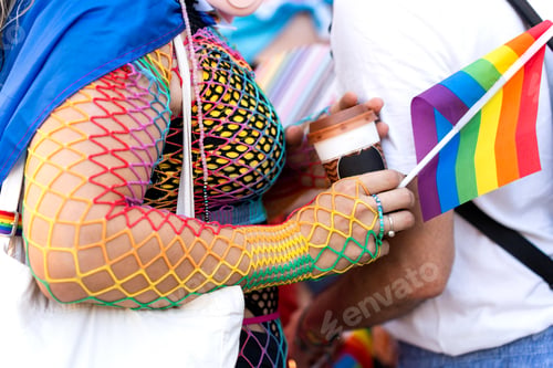 Preview: Woman wearing rainbow clothes holding coffee and lgbt flag at pride parade