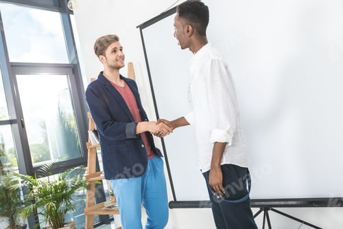 Preview: multiethnic young businessmen shaking hands after meeting in office