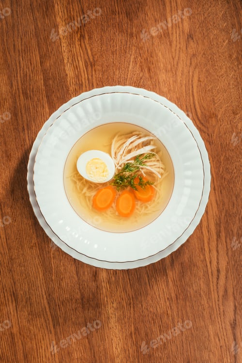 Preview: Top view of chicken soup with vegetables and egg in white plate on wooden table