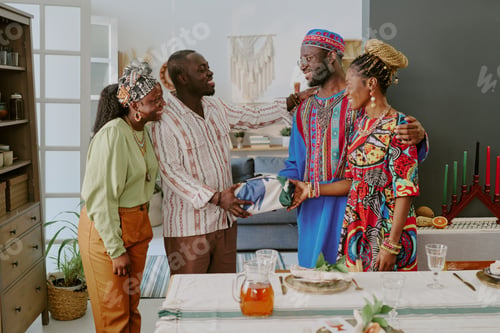 Preview: Group of Black Adults Celebrating Kwanzaa and Exchanging Gifts Indoors