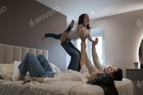 Preview: Happy parents lifting daughter while lying on bed in bedroom