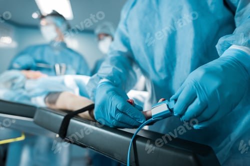 Preview: cropped image of doctor wearing pulse oximeter on patient finger in operating room