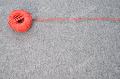 Preview: Ball of red yarn with a loose string stretching to the side on a gray background with copy space