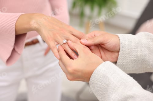 Preview: Making marriage proposal. Man putting engagement ring onto his girlfriend's finger at home, closeup
