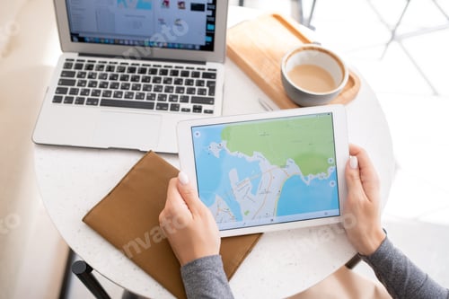 Preview: Young woman holding touchpad with map on its display while working by table