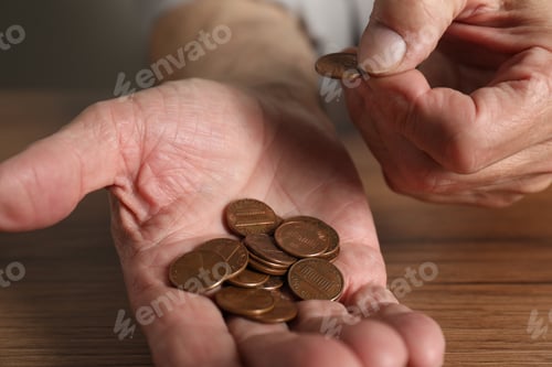 Preview: Senior man counting coins at wooden table, closeup. Financial problems