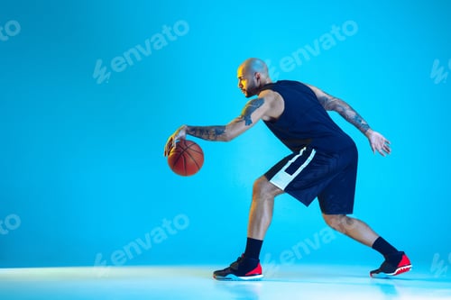 Preview: Young basketball player training isolated on blue studio background in neon light
