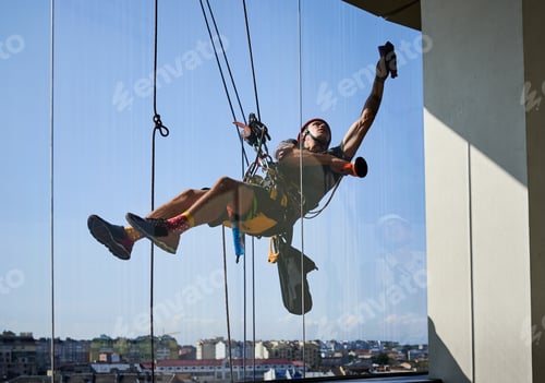 Preview: Industrial mountaineering worker cleaning window outside building.