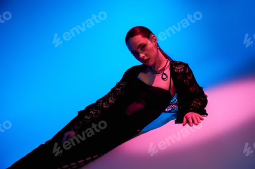 Preview: Stylish young woman poses gracefully in studio with vibrant pink and blue lighting