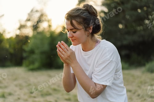 Preview: Woman closed her eyes, praying in a field during beautiful sunset.