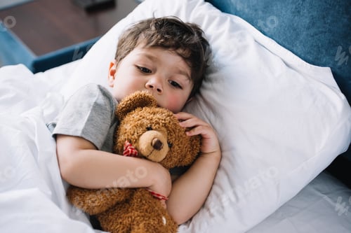 Preview: cute kid lying in bed with teddy bear at home