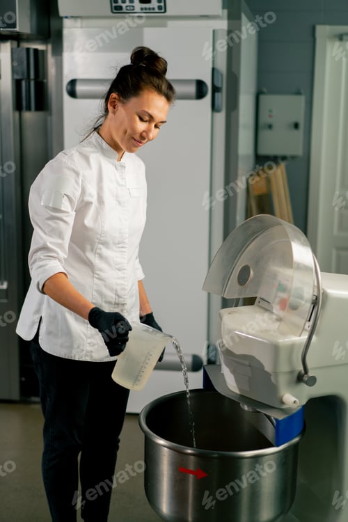 Preview: Woman baker putting dough into kitchen planetary mixer for mixing to prepare delicious bread