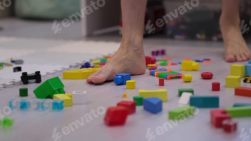 Preview: barefoot man walks among the scattered toys. Foot stepping on children's toys.
