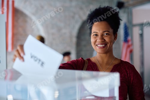 Preview: Happy black woman voting at polling place during US elections and looking at camera.