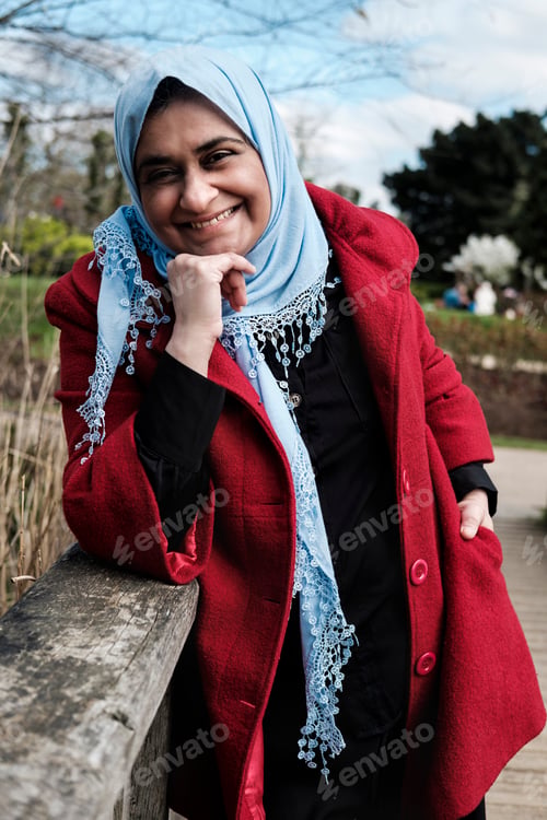 Preview: Muslim mature woman wearing hijab posing smiling in a banister in a park in London.