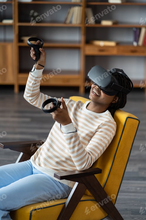 Preview: Happy young african american woman wearing virtual reality goggles playing video games at home