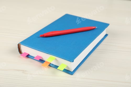 Preview: Book with colorful tabs and pen on light wooden table, closeup