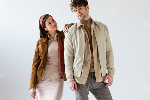 Preview: Beautiful girl in autumn outfit posing near stylish man looking at camera on grey