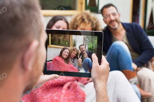 Preview: Over the shoulder view of man photographing friends on digital tablet