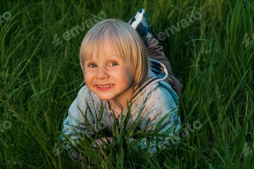 Preview: little kid toddler boy lying on grass lawn at home yard garden.Child in backyard.Happy childhood