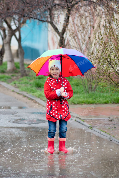 Preview: A cute little girl in a red cape, red boots and a white hat jump in puddles and has a fun.