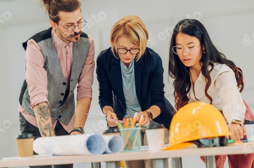 Preview: Multiracial team of architects having a meeting while using blueprints