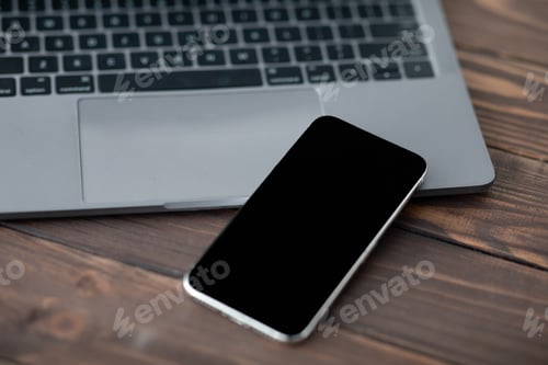 Preview: Modern smartphone with black blank screen placed near laptop computer, closeup. Mockup for your