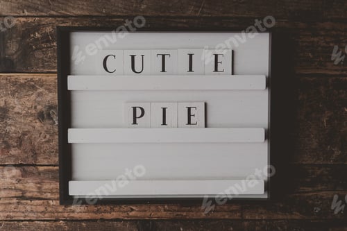 Preview: White sign with a writing "Cutie pie" on it on a wooden brown background