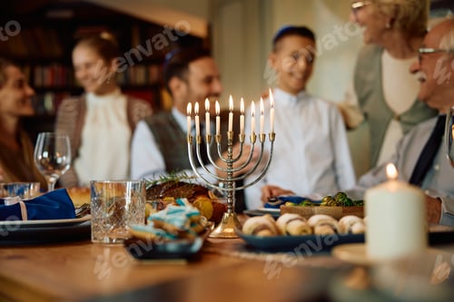 Preview: Lit menorah with Jewish extended family in the background on Hanukkah.