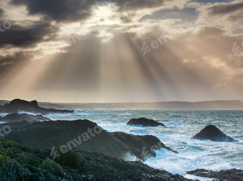 Preview: Heavenly light pierces through stormy skies over a rugged seascape