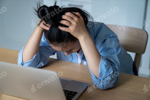 Preview: Stressed woman sitting at desk with laptop holding head in hands having online business problems